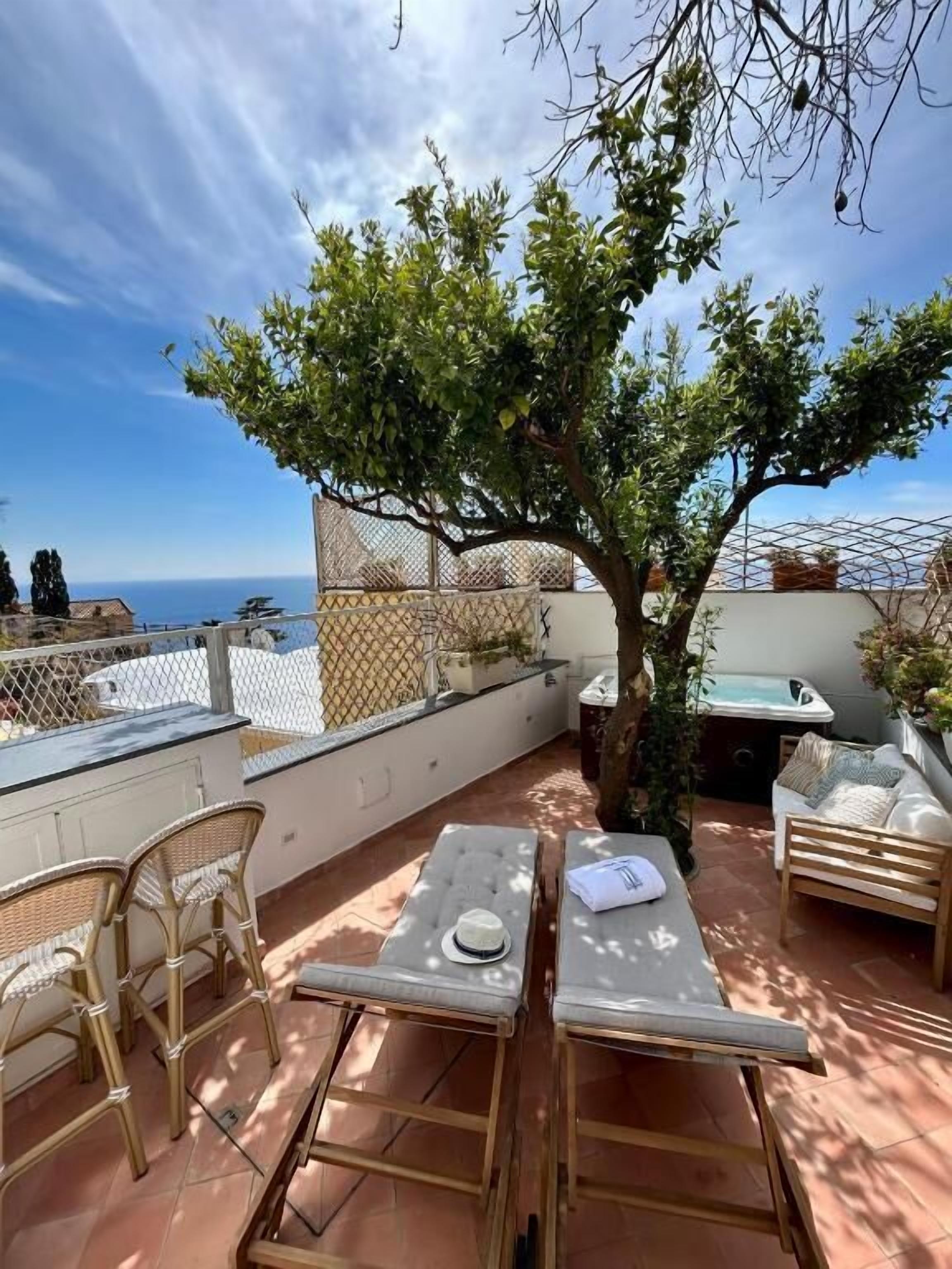 A terrace with wicker furniture, a table, and a tree providing shade.