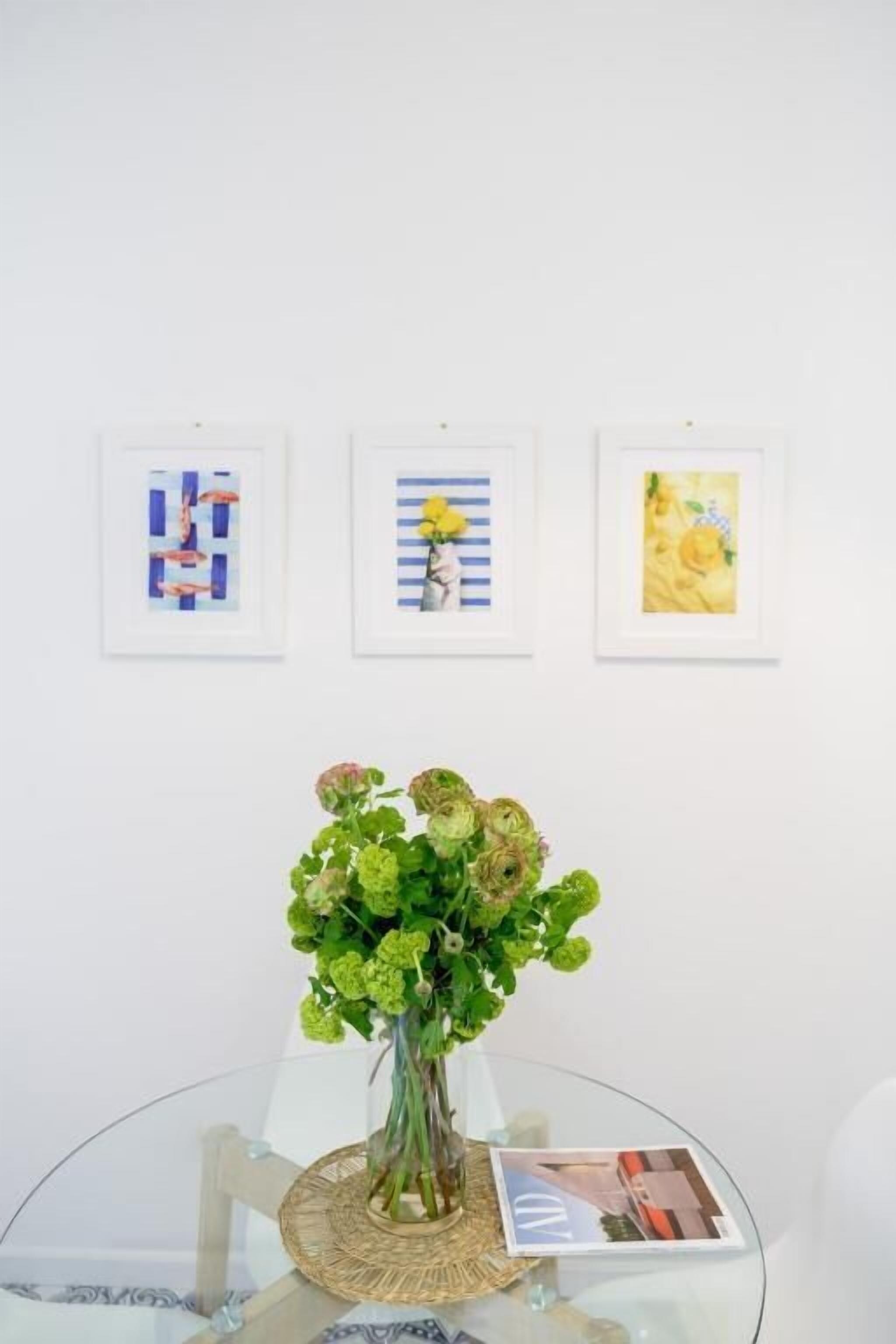 A glass table with a vase of flowers, three framed artworks, and a magazine on the table.