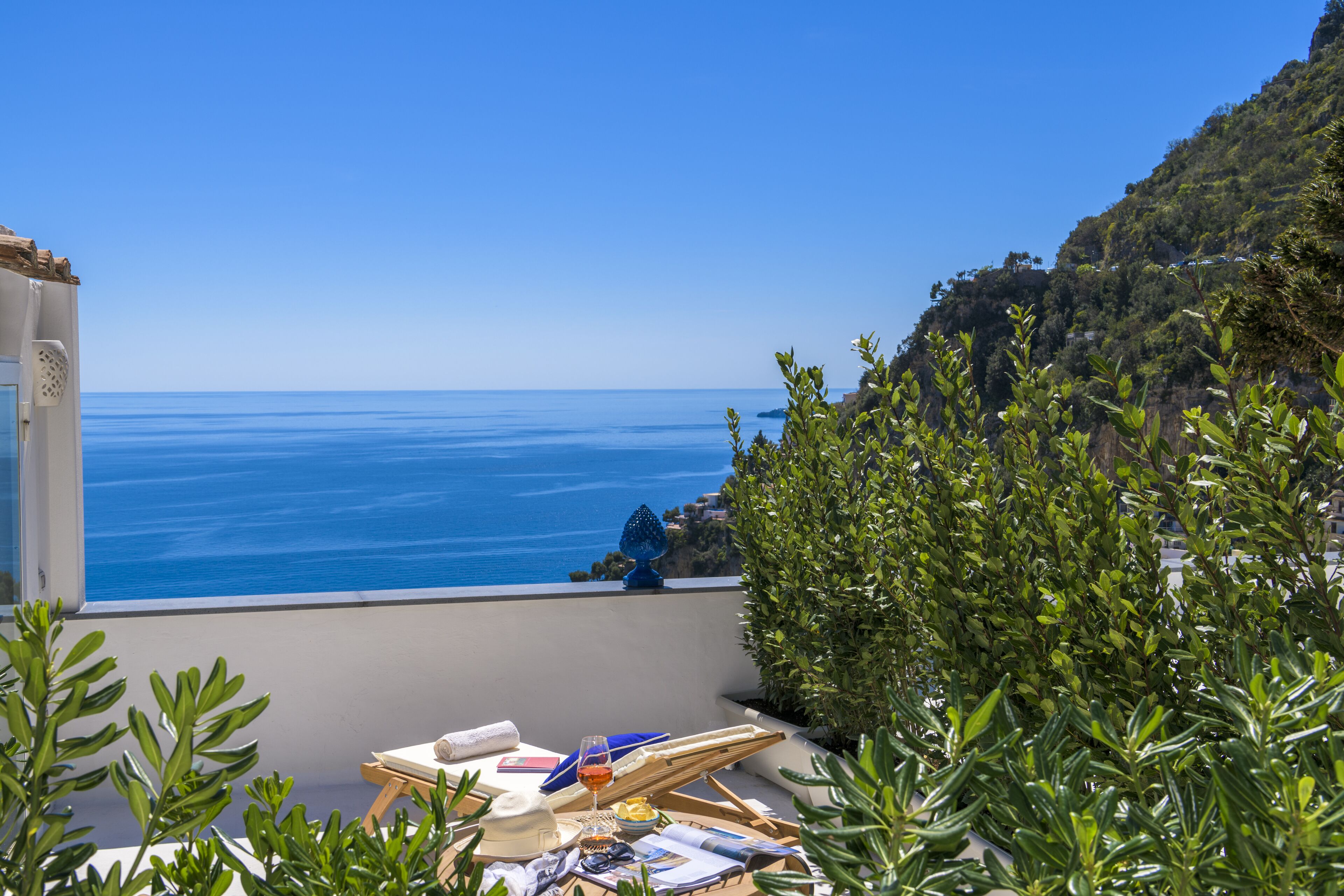 Una terraza con vista al mar, una mesa con una silla y vegetación.