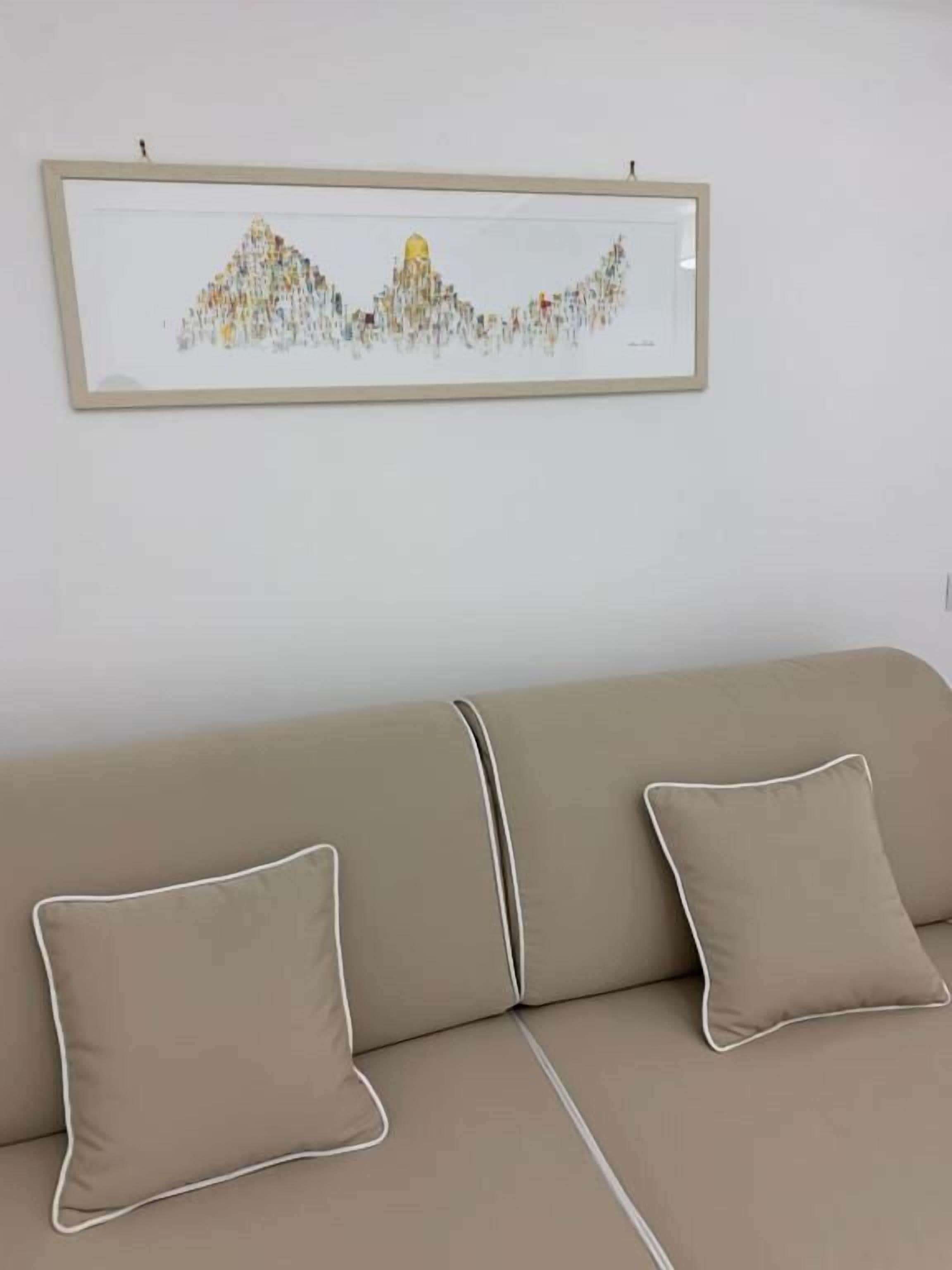 A beige sofa with two pillows and a framed artwork above it.