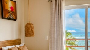 Quarto de hotel com duas camas, um lustre, um quadro e vista para o oceano.