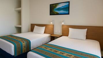 Een hotelkamer met twee bedden, elk met een houten hoofdbord en witte beddengoed. Daarboven hangt een schilderij van een landschap aan de muur.