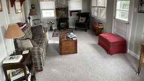 A cozy living room with a plaid sofa, a wooden coffee table, a fireplace, and a red ottoman. - Cozy cottage located at our winery at the base of Old Rag  and Shenandoah Park. (Sperryville)