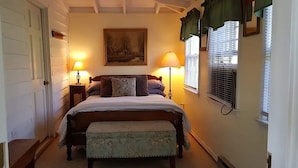 A bedroom with a bed, two bedside lamps, a bench, a painting on the wall, and a window with blinds. - Cozy cottage located at our winery at the base of Old Rag  and Shenandoah Park. (Sperryville)