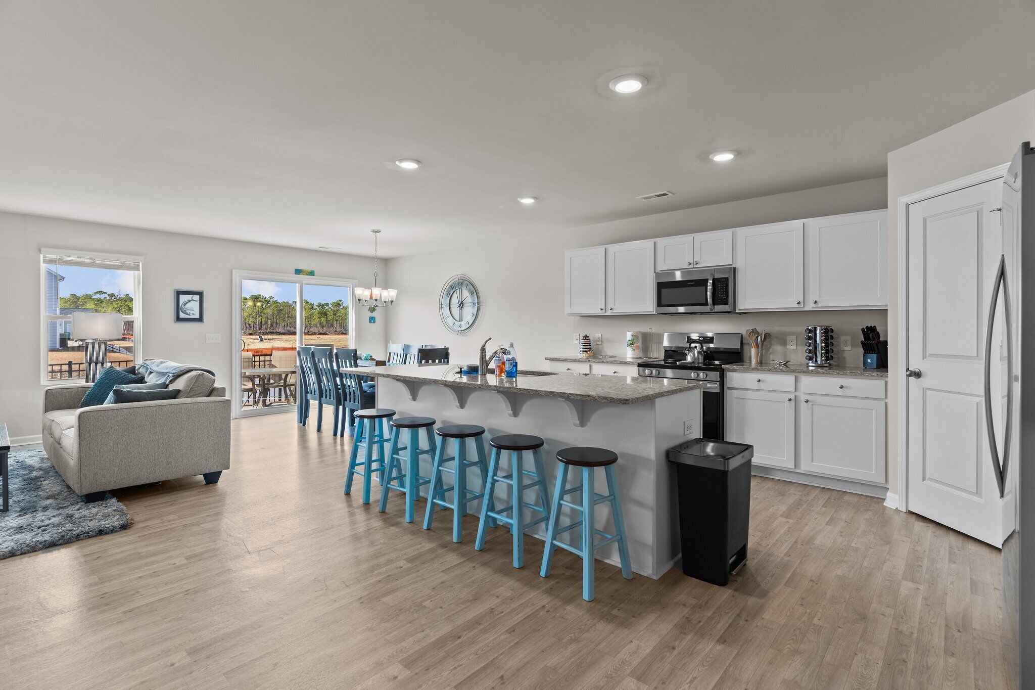 A modern kitchen with white cabinets, a central island with stools, a microwave, and a refrigerator.