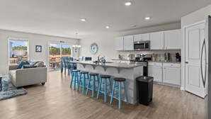 Una cocina moderna con armarios blancos, una isla central con taburetes, microondas y refrigerador.