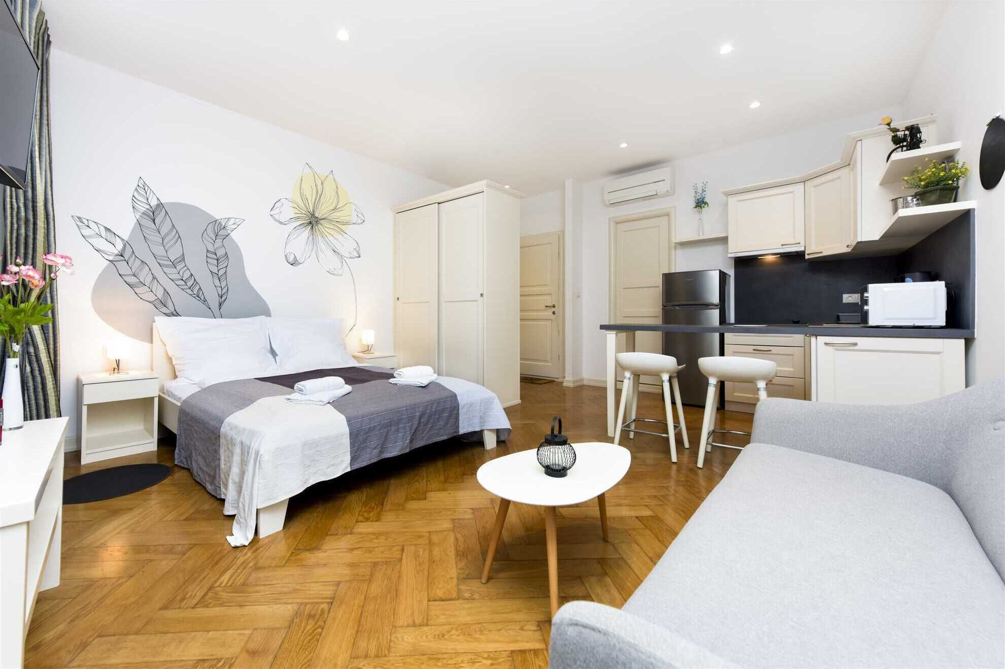 Un espace de vie moderne et compact comprenant un lit, un canapé, un petit coin repas et une kitchenette.