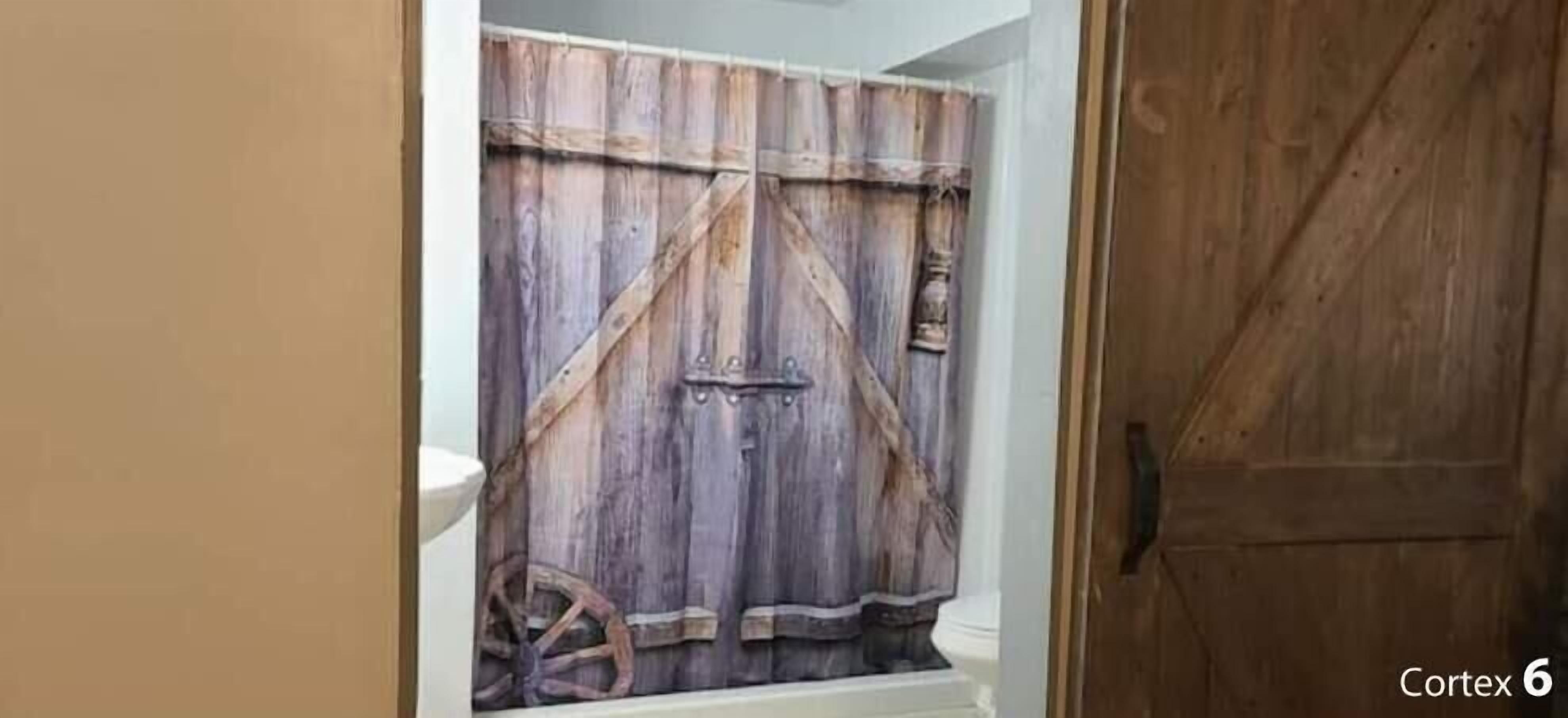 Un bagno con una porta in legno rustica, un lavandino bianco e una tenda da doccia.