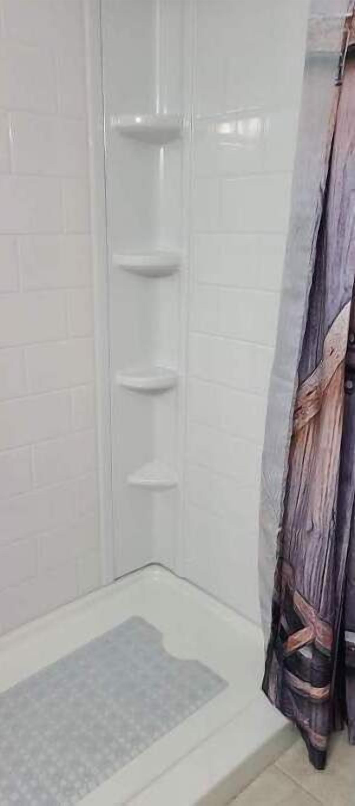 A shower area with a tiled wall and a shower curtain.