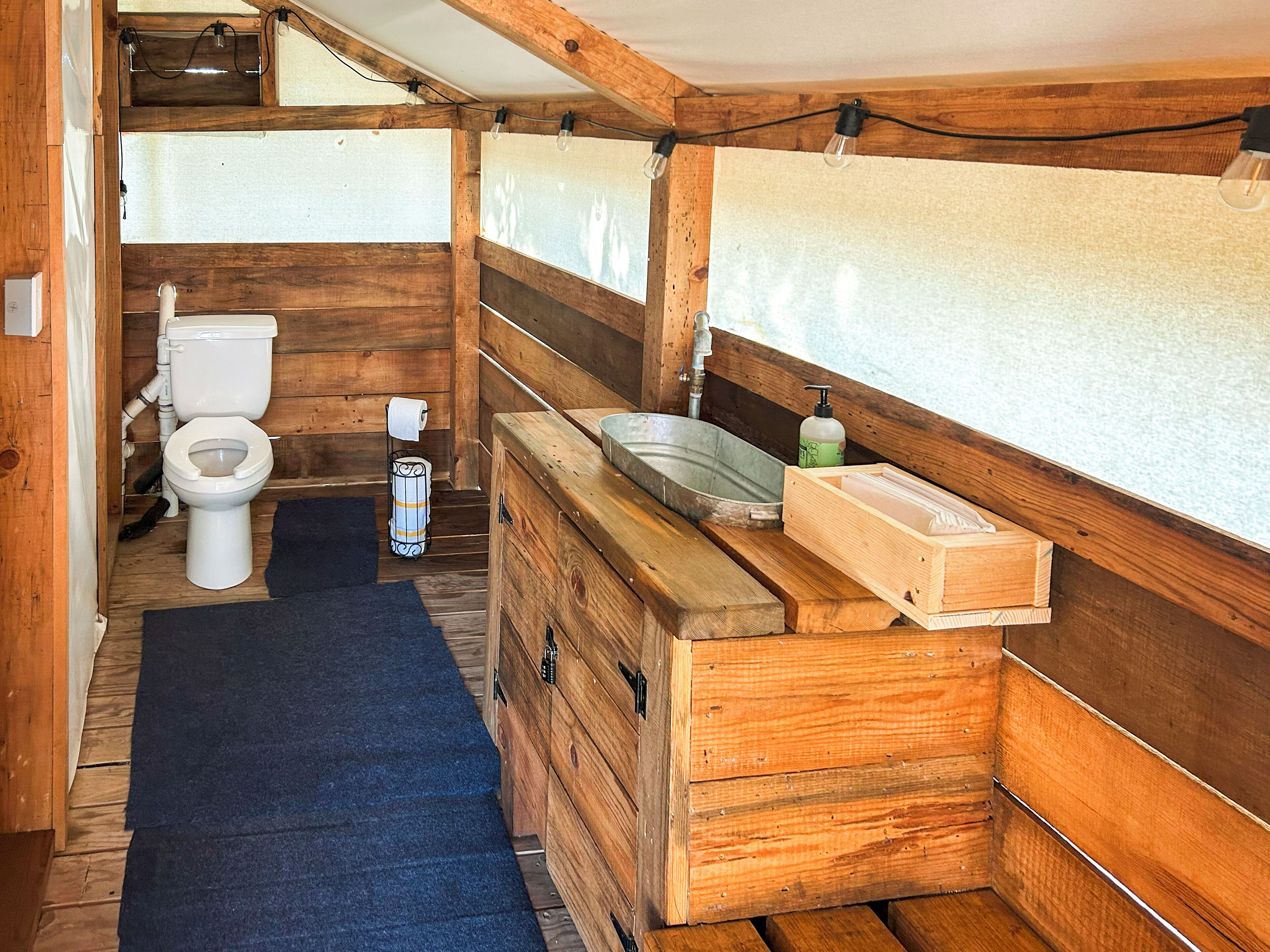 Een klein houten badkamertje met toilet, wastafel en een opbergkastje.