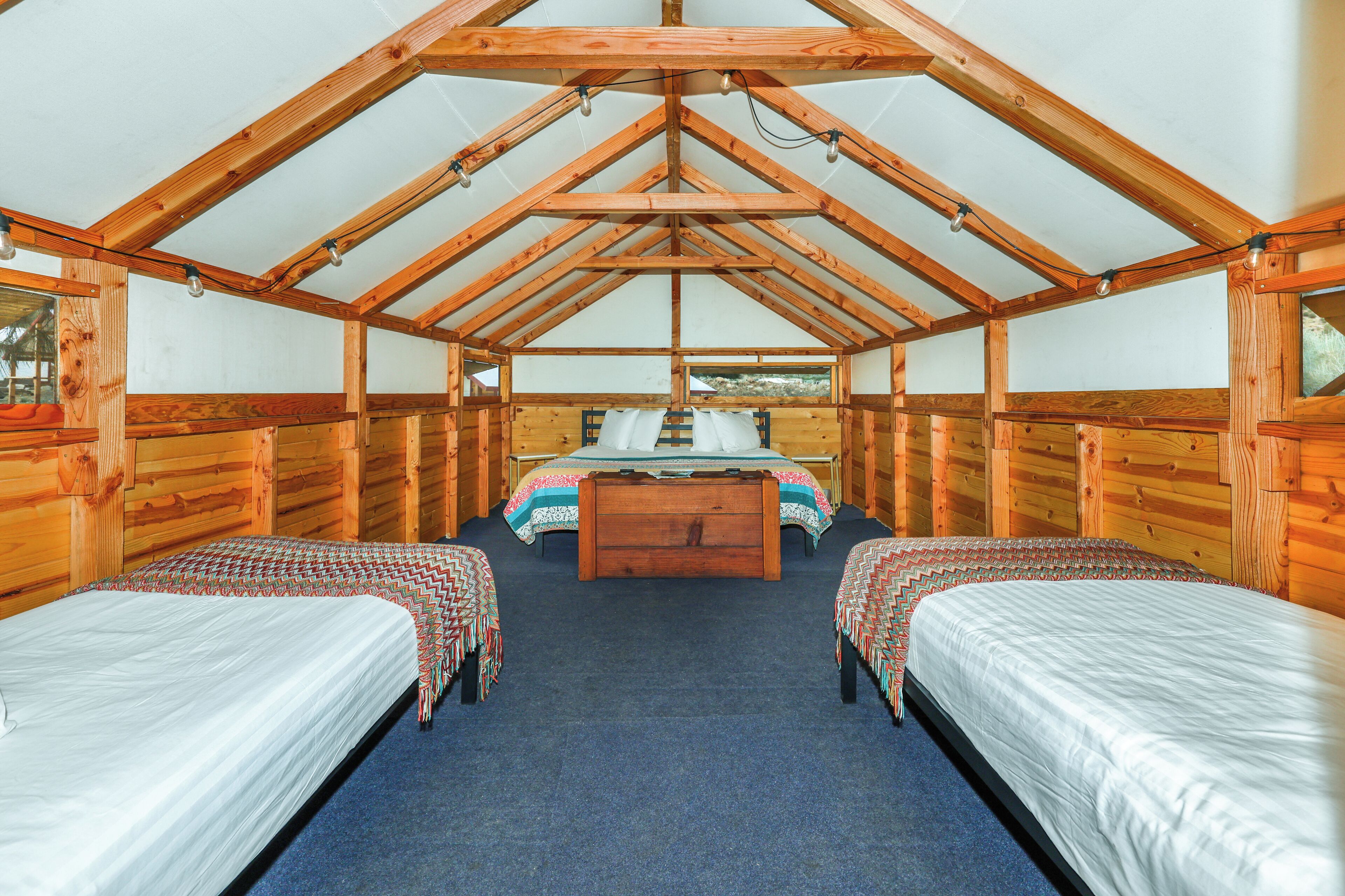A cabin with two single beds, a central bed, and a wooden ceiling structure.