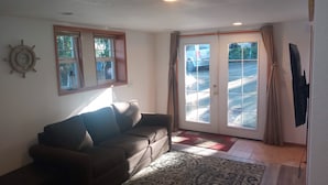 A living room with a sofa, a patterned rug, a wall clock, and a sliding glass door leading outside. - Bremerton Sheltered Waterfront (Bremerton)