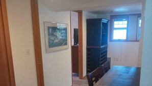A dining area with a long wooden table and chairs, a framed picture on the wall, and a window with blinds. - Bremerton Sheltered Waterfront (Bremerton)