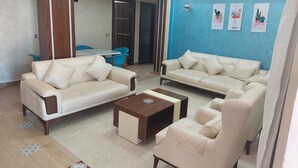 Una sala de estar con dos sofás beige, una mesa de centro de madera y una pared azul decorada con plantas en macetas.