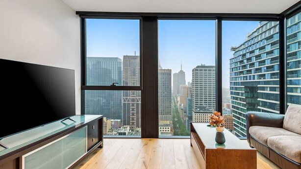 A modern living room with a large TV, a coffee table, and a sofa. - Stunning City Views 2B2B apt in CBD (Melbourne)
