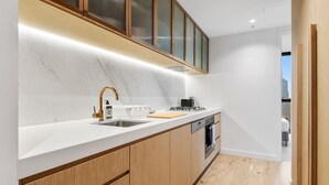 A modern kitchen with a white countertop, wooden cabinets, a stainless steel sink, and a built-in oven. - Stunning City Views 2B2B apt in CBD (Melbourne)