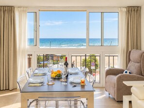 A dining area with a view of the ocean, a table set with plates, glasses, and a bottle, and a sofa in the foreground. - Cubo's Estepona Oceanview Apartment & Free Parking / beachfront / free wifi / parking included (Estepona)