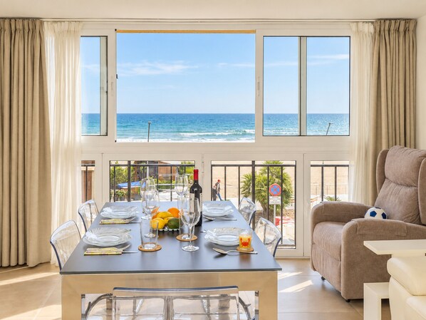 A dining area with a view of the ocean, a table set with plates, glasses, and a bottle, and a sofa in the foreground.