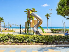 Un parque infantil con tobogán y estructuras para escalar cerca de una playa.