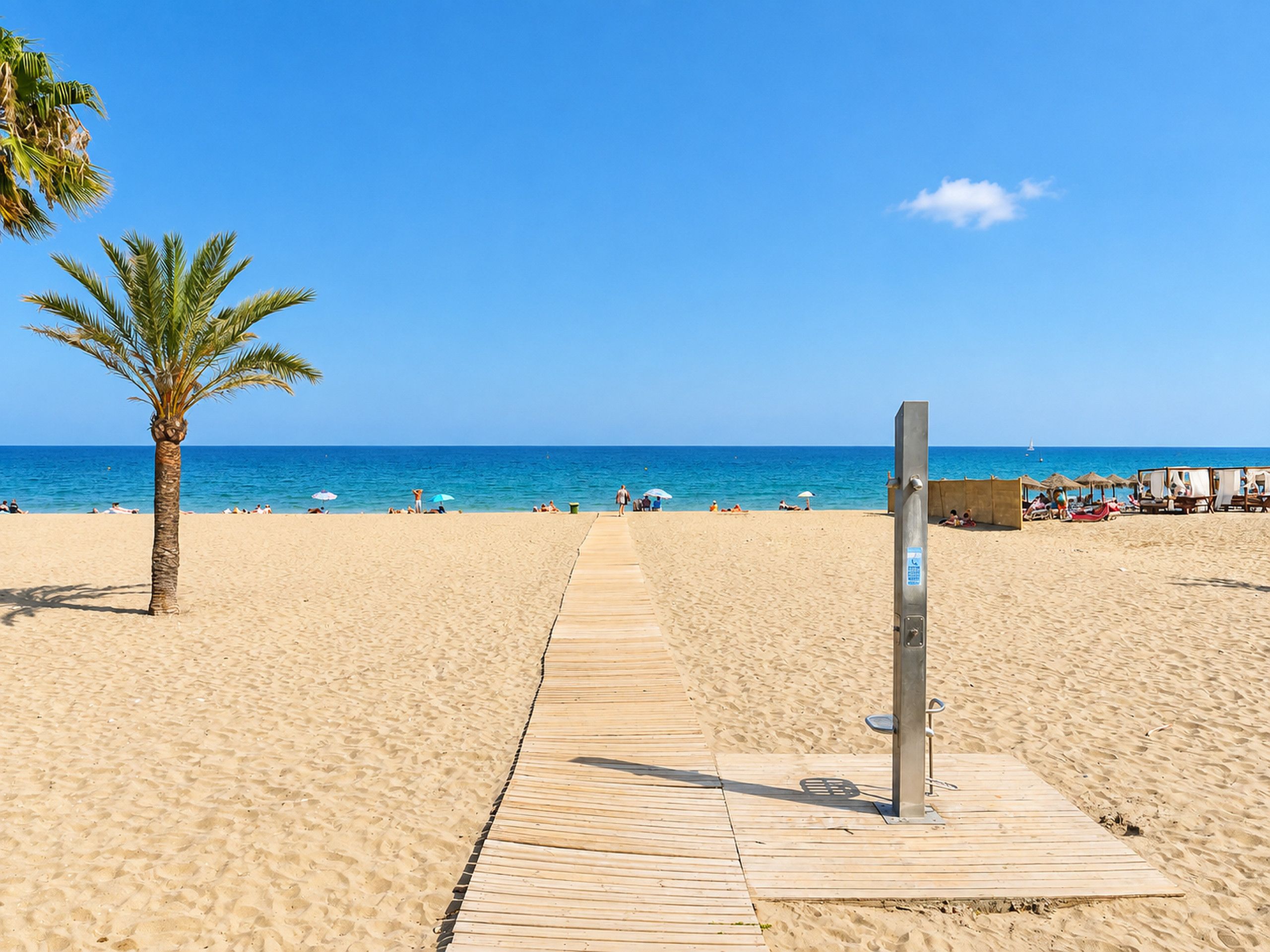 A sandy beach with a wooden walkway leading to the sea, palm trees, and beach umbrellas.