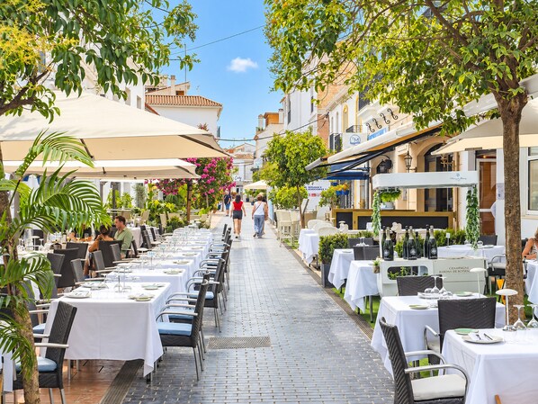 An outdoor dining area with tables and chairs, surrounded by buildings and trees.