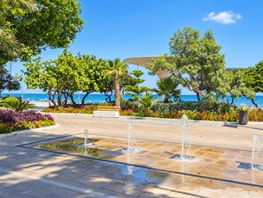 A public square with a fountain, benches, and a view of the sea.