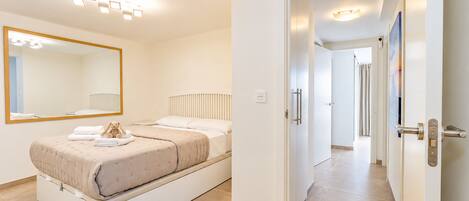 Quarto moderno com cama, um espelho grande e um corredor que dá para outro ambiente.