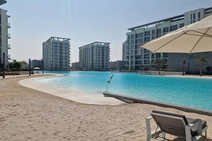 A swimming pool with a sandy beach area, surrounded by modern buildings. - 1BR Luxury Oasis in Dubai (Dubai)