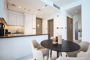 A modern kitchen with white cabinetry, a black countertop, and a round dining table with two chairs. - 1BR Luxury Oasis in Dubai (Dubai)
