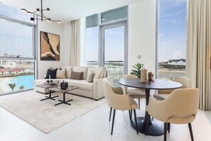 A modern living room with a sofa, coffee table, and dining table, large windows with a view of a bridge and buildings, and a pool. - 1BR Luxury Oasis in Dubai (Dubai)