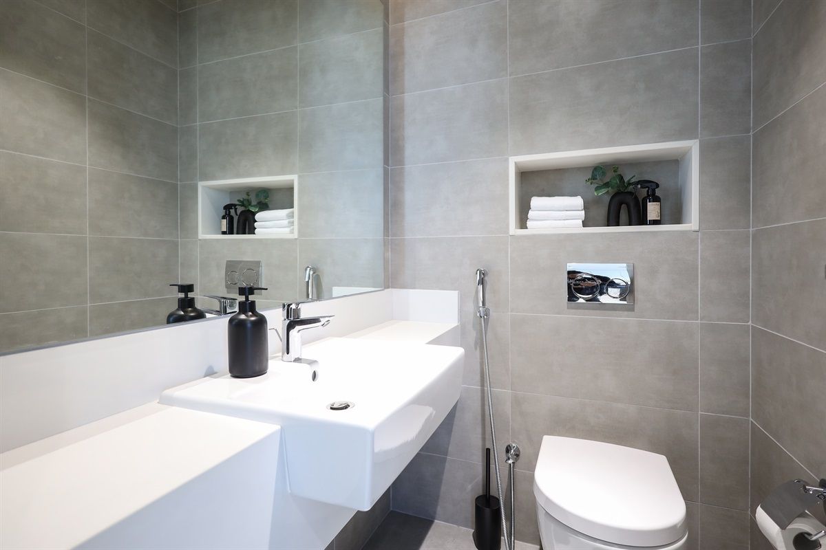 A modern bathroom with a large white sink, a separate basin, a toilet, and built-in shelves with toiletries.