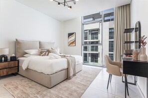 A modern bedroom with a large bed, a desk, and a view of a building through large windows. - 1BR Luxury Oasis in Dubai (Dubai)