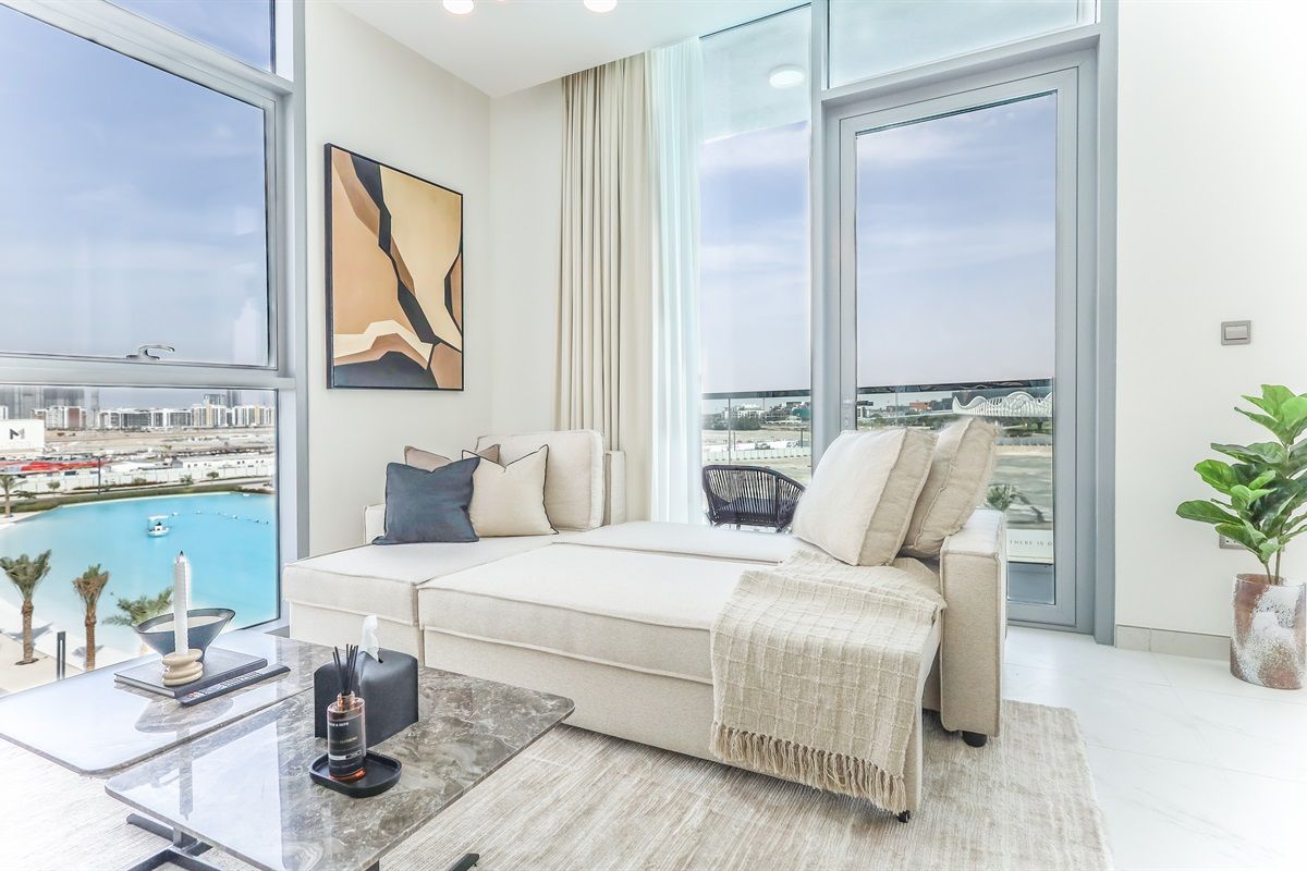 A modern living room with a large window, a sofa, a coffee table, and a view of a cityscape.