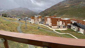 Et bjergrigt område med et moderne bykompleks, herunder et hotel med flere etager og altaner, omgivet af naturlig skønhed.