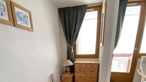 Et soveværelse med seng, kommode, lampe og et vindue med gardiner.
