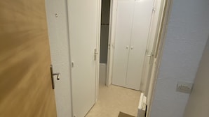 En smal gang med en trædør til venstre, en hvid dør i midten og en hvid dør til højre. En loftlampe er synlig over døren i midten.
