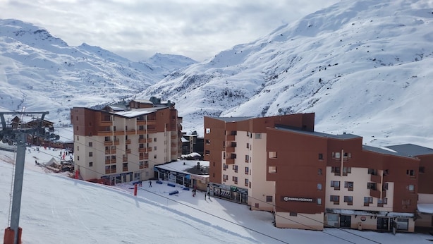 Et sneklædt bjergresort med høje bygninger, skilifte og en ski-piste.