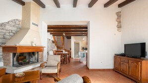 A spacious living area with a fireplace, wooden furniture, a television, and a kitchen in the background.