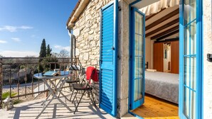 A stone building with blue shutters, a wooden deck, a table with chairs, and a bed inside.