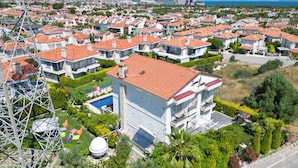 A residential area with multiple houses featuring red-tiled roofs, a swimming pool, and lush greenery.
