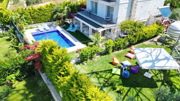 A pool with lounge chairs, a covered patio, and a garden with various plants and seating areas.