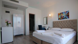 A hotel room with a bed, a wardrobe, a desk, and a painting on the wall.