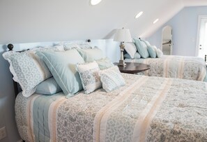 Une chambre avec deux lits, chacun agrémenté de draps à motifs et d’une table de chevet avec une lampe.