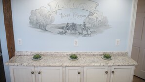 A kitchen with a granite countertop, white cabinets, and a mural welcoming to the Stable Cottage West Manor Estate.