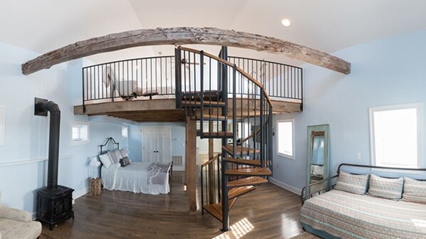 Une pièce spacieuse avec un escalier en bois menant à une mezzanine, un grand lit et un coin salon confortable.