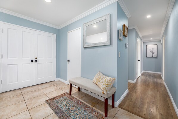 A hallway with a bench, a door, a mirror, and a rug.