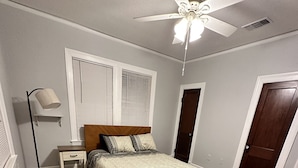 A bedroom with a wooden floor, a bed with patterned bedding, a nightstand, a floor lamp, a ceiling fan, and a door. - TigerTown Retreat. Downtown Baton Rouge and 5 minutes to LSU. (Baton Rouge)