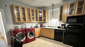 A kitchen with wooden cabinets, a ceiling fan, a washing machine, and a dining area with a table and chairs. - TigerTown Retreat. Downtown Baton Rouge and 5 minutes to LSU. (Baton Rouge)
