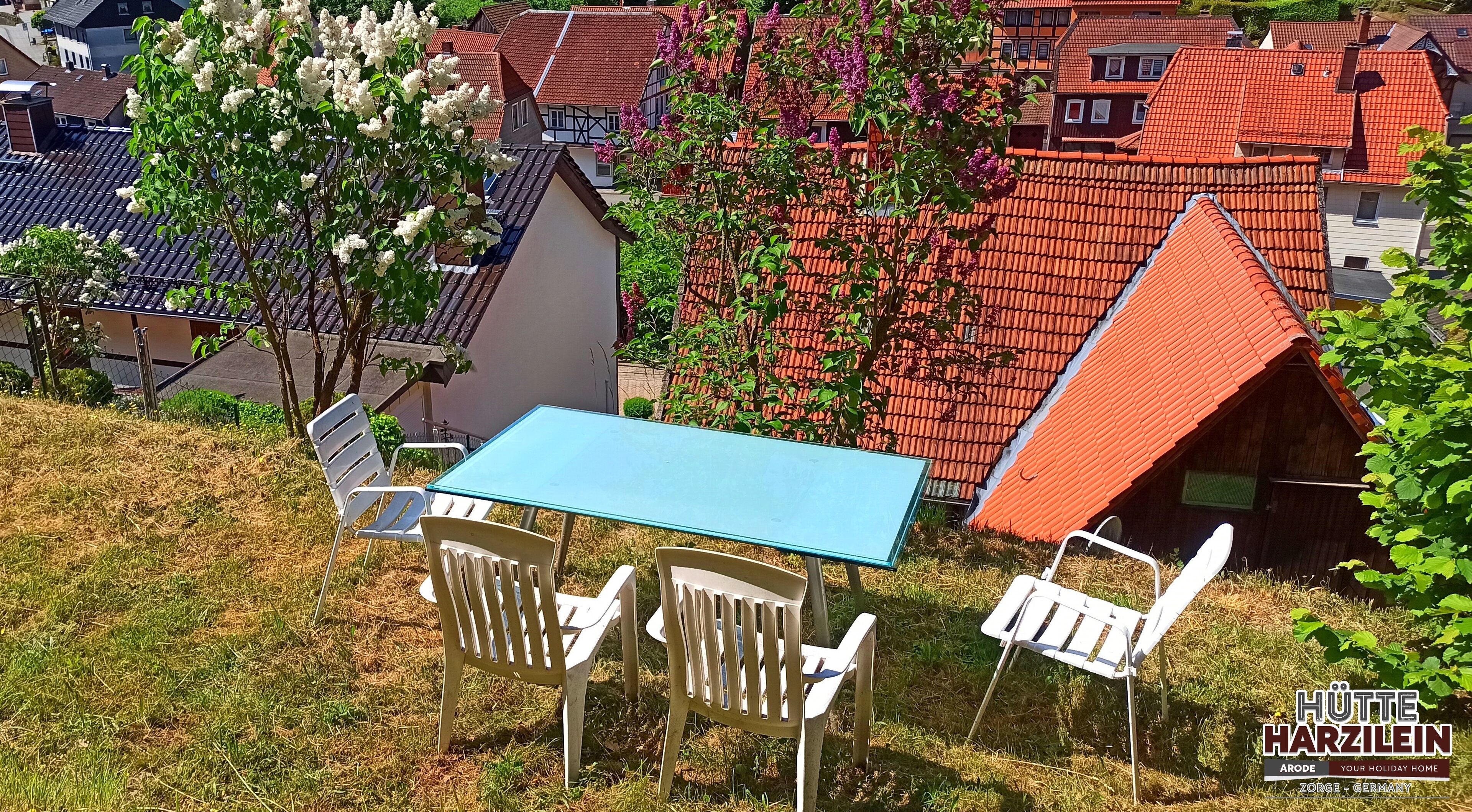 A table and chairs set on a grassy slope with a view of traditional houses with red roofs.