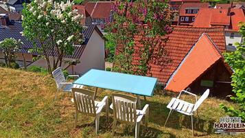 A table and chairs set on a grassy slope with a view of traditional houses with red roofs.
